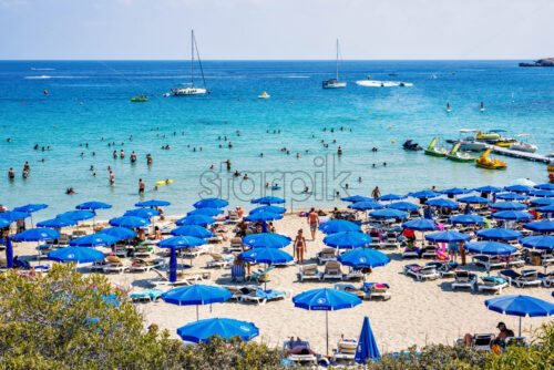 LIMASSOL, CYPRUS – SEPTEMBER 14, 2017: Daylight view to Konnos beach with people relaxing in water, on sand. Boats riding on blue water. Bright clear sky. Negative copy space, place for text. - Starpik