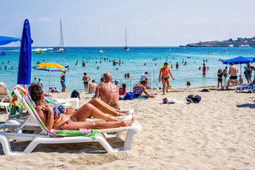 LIMASSOL, CYPRUS – SEPTEMBER 14, 2017: Daylight view to Konnos beach with people relaxing in water, on sand. Boats riding on blue water. Bright clear sky. Negative copy space, place for text. - Starpik