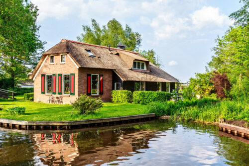 Local river from bottom in a sunny day. Trees, traditional houses and bright blue sky with clouds on background. Negative copy space, place for text. Giethoorn, Netherlands - Starpik