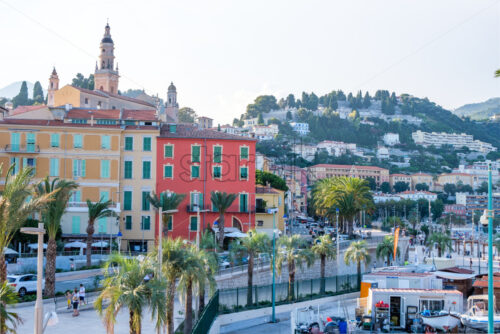 MENTON, FRANCE – AUGUST 06, 2018: City at sunset with cars riding on road. Colorful buildings and mountains - Starpik