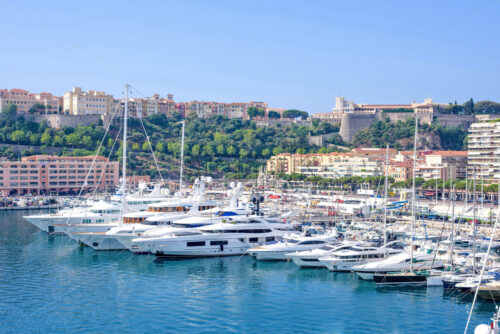 MONACO, FRANCE – JUNE 28, 2017: Daylight sunny view to parked luxury yachts and tall buildings constructed in city. Bright blue clear sky. - Starpik