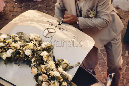 Man at wedding opening the mercedes benz car at a church, flowers - Starpik