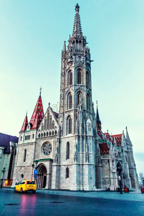 Matthias Church from bottom at sunset. Cold blue sky on background. Smooth textures. Taxi with lights on at entrance. Negative copy space, place for text. Budapest, Hungary - Starpik