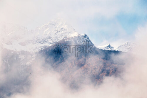 Mountains covered with snow on top. View through clouds. Chiavenna, Italy - Starpik