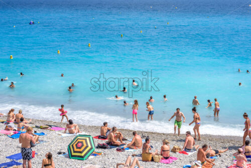 NICE, FRANCE – JUNE 27, 2017: Beautiful daylight view. Blue water with people walking on sand. - Starpik