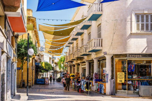 NICOSIA, CYPRUS – SEPTEMBER 14, 2017: Daylight view to Ledra street with people walking and exploring shops and restaurants. Sun shades between buildings. - Starpik