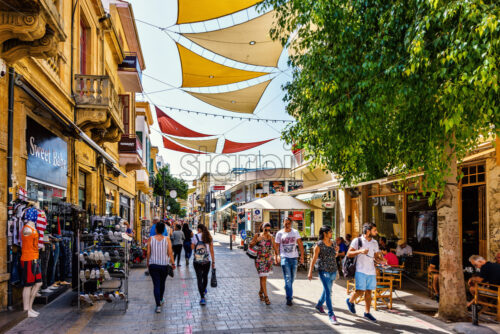 NICOSIA, CYPRUS – SEPTEMBER 14, 2017: Daylight view to Ledra street with people walking and exploring shops and restaurants. Sun shades between buildings. - Starpik