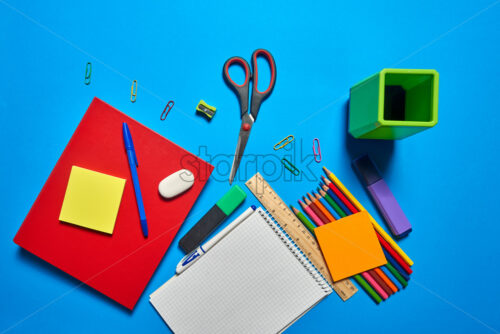 Overhead shot of school and office supplies on vibrant blue background - Starpik