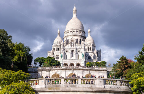 PARIS, FRANCE – OCTOBER 01, 2018: Long view to Sacre Coeur Basilica in Paris. Lots of tourists with plenty of attractions. Rainy day with sunshine making a lot of contrast on the building - Starpik