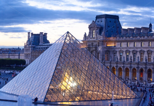 PARIS, FRANCE – OCTOBER 03, 2018: Louvre Museum at sunset. People on promenade. Yellow sunshine reflecting on building - Starpik