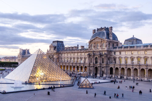 PARIS, FRANCE – OCTOBER 03, 2018: Louvre museum at sunset. Magenta look in the horizont. Tourists walking in the square. Soft clouds in the sky - Starpik