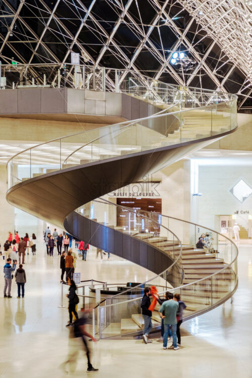 PARIS, FRANCE – OCTOBER 03, 2018: Spiral staircase in Louvre museum. People leaving the place at night. End of the day idea - Starpik