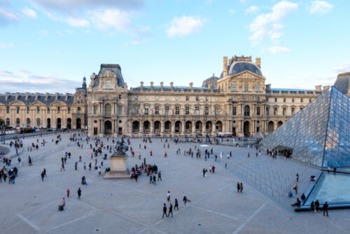 PARIS, FRANCE – OCTOBER 03, 2018: Wide angle aerial view to Louvre museum. Blue sky with some clouds. Shot at sunset. Tourists leaving on of the most important hystorical place in Paris - Starpik