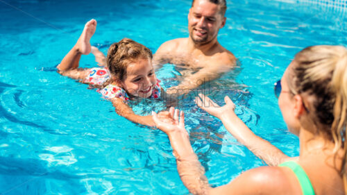 Parents teaching their daughter swimming in the pool - Starpik