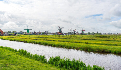 Picturesque landscape of Zaanse Schans in a cloudy day. Bright sky on background. Green grass and light reflecting on water. North Holland - Starpik