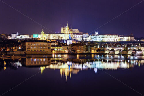 Prague Castle and Charles Bridge at night with lights glowing and reflecting on water. Negative copy space, place for text. Czech Republic - Starpik