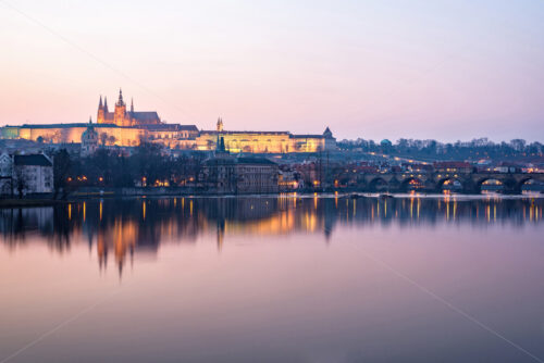 Prague Castle and Charles Bridge at sunset with lights glowing and reflecting on water. Negative copy space, place for text. Czech Republic - Starpik