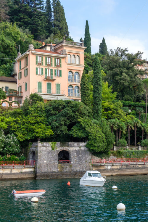 Rich villa on shore of Lake Como with yacht and boat parked in front. Varenna, Italy - Starpik