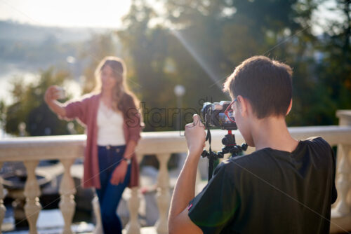 Shot of a photographer shooting a beautiful caucasian woman on a camera with a tripod - Starpik