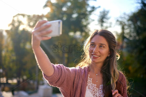 Shot of gorgeous and smiling caucasian woman taking selfie with park and stairs in the background - Starpik