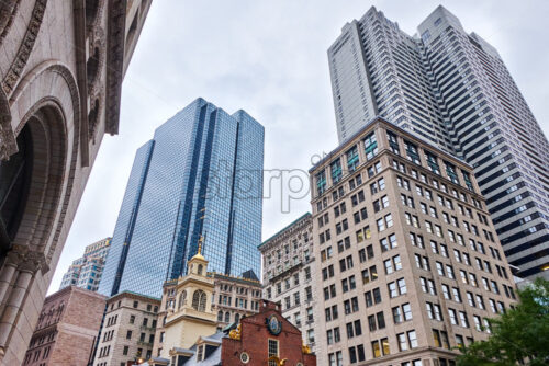 Shot of multiple modern and aged, high and low building behind and above the Old Sate House in Boston, the sky is gray and cloudy - Starpik