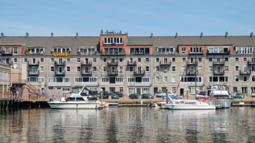 Shot of several moored yachts on the smooth surface of the water with beautiful residential building and blue clear sky in the background located in Boston - Starpik