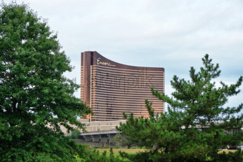 Shot of the Encore Boston Harbor visible between two lush trees with gray and cloudy sky in the background - Starpik