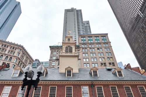 Shot of the Old State House in Boston made from the side with multiple modern and aged buildings. The weather is cloudy - Starpik