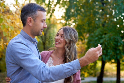 Shot of the beautiful smiling couple taking selfie and looking at each other with autumn yellow and green leaves in the background - Starpik