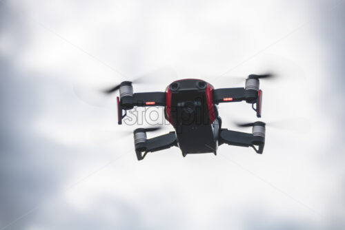 Small red drone in the air with the camera looking downwards. Dramatic looking sky in the background - Starpik