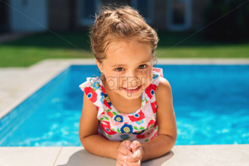 Smiling girl holding on to the side of the pool and looking into the camera - Starpik