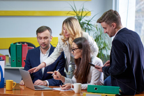 Team of mature women and men at meeting table discussing a business plan with laptop computer in office. Window on background - Starpik