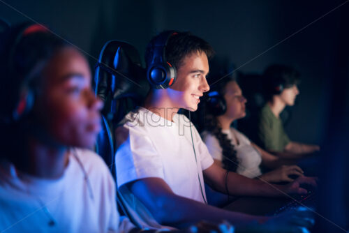 Teen smiling boy in headset playing video games in video game club with blue and red illumination - Starpik