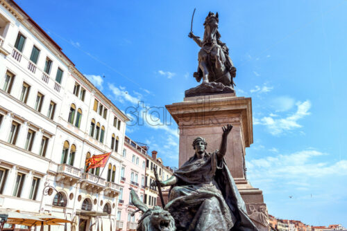 VENICE, ITALY – APRIL 02, 2017: Daylight view from bottom to Equestrian Statue of King Victor Emmanuel II in Riva degli Schiavoni waterfront. People walking and historic buildings on background. - Starpik