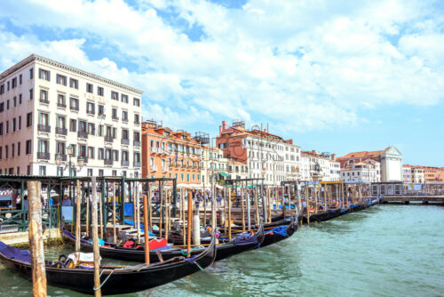 VENICE, ITALY – APRIL 02, 2017: Daylight view to parked boats, historic architecture buildings and people walking on Riva degli Schiavoni waterfront. Bright blue sky with birds, clouds. Energetic mood - Starpik