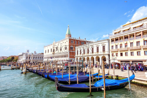 VENICE, ITALY – APRIL 02, 2017: Daylight view to parked boats, historic architecture buildings and people walking on Riva degli Schiavoni waterfront. Bright blue sky with birds, clouds. Energetic mood - Starpik