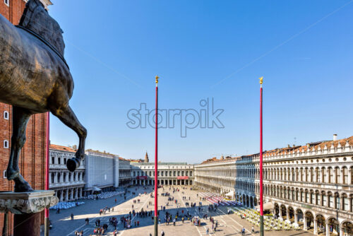 VENICE, ITALY – APRIL 03, 2017: Daylight view from Horses of Saint Mark to square with tourists walking and taking photos. Renaissance style buildings and open-air restaurants. Bright blue clear sky - Starpik