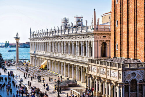 VENICE, ITALY – APRIL 03, 2017: Daylight view to Marciana Library renaissance style facade and campanile entrance from Saint Mark’s square overcrowded with tourists. Bright blue clear sky - Starpik