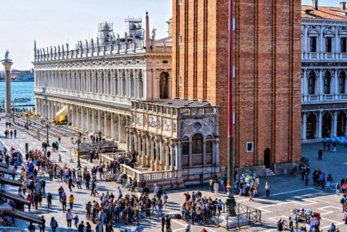 VENICE, ITALY – APRIL 03, 2017: Daylight view to Marciana Library renaissance style facade and campanile entrance from Saint Mark’s square overcrowded with tourists. Bright blue clear sky - Starpik