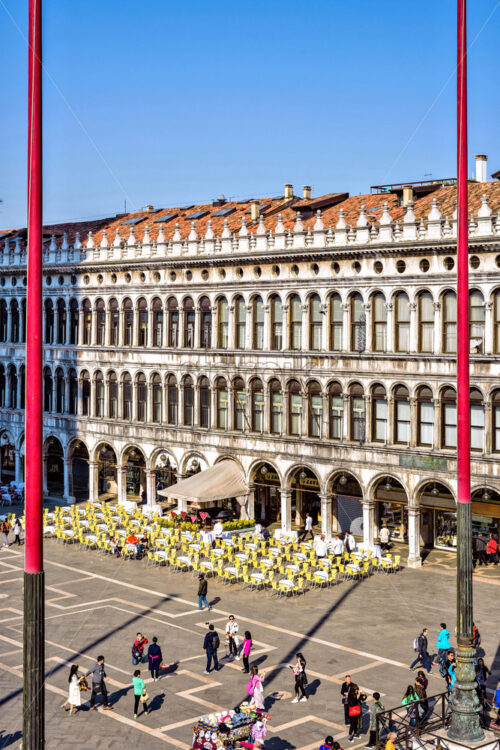 VENICE, ITALY – APRIL 03, 2017: Daylight view to Saint Mark’s square with tourists walking and taking photos. Renaissance architecture style buildings and open-air restaurants. Bright blue clear sky - Starpik