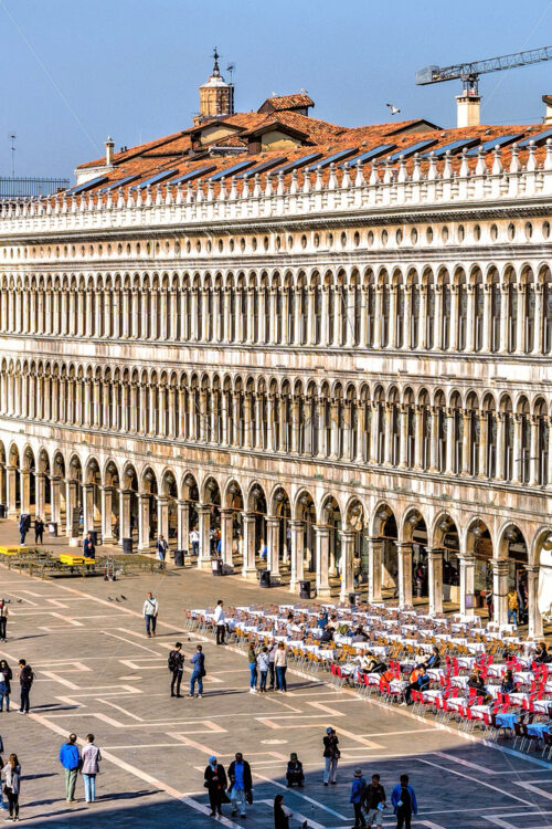 VENICE, ITALY – APRIL 03, 2017: Daylight view to Saint Mark’s square with tourists walking and taking photos. Renaissance architecture style buildings and open-air restaurants. Bright blue clear sky - Starpik