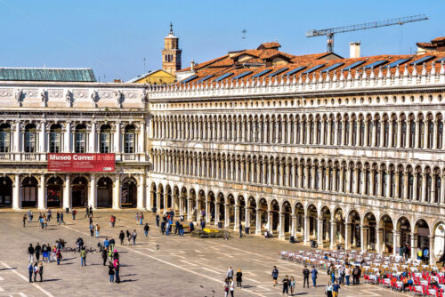 VENICE, ITALY – APRIL 03, 2017: Daylight view to Saint Mark’s square with tourists walking and taking photos. Renaissance architecture style buildings and open-air restaurants. Bright blue clear sky - Starpik