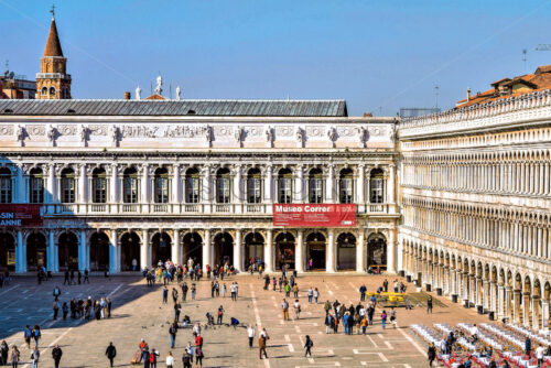 VENICE, ITALY – APRIL 03, 2017: Daylight view to Saint Mark’s square with tourists walking and taking photos. Renaissance architecture style buildings on background. Bright blue clear sky - Starpik