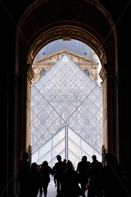 Vertical shot to people entering through the gates of Louvre. Symetric shot. Touristic locations in France - Starpik