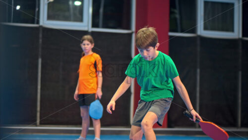 Video A boy and a girl training to play pickleball on a blue, inside court - Starpik Stock