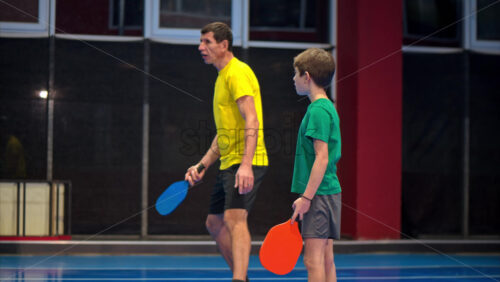 Video A man and a child playing pickleball on a blue, inside court - Starpik Stock