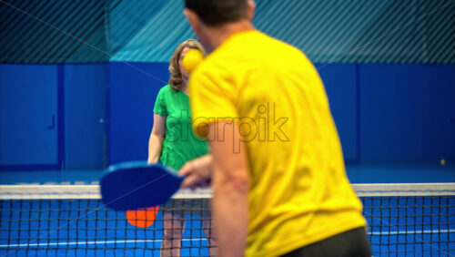 Video A man and a woman playing pickleball on a blue, inside court - Starpik Stock