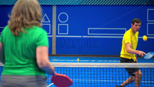 Video A man and a woman playing pickleball on a blue, inside court - Starpik Stock