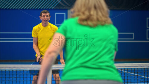 Video A man and a woman playing pickleball on a blue, inside court - Starpik Stock