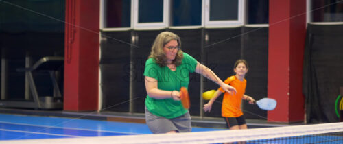 Video A woman and a child playing pickleball on a blue, inside court - Starpik Stock